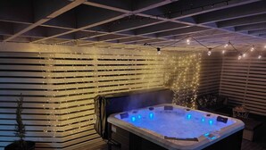 Uma banheira de hidromassagem em um quarto com ripas de madeira nas paredes e luzes de corda.