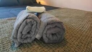 Cama bem arrumada com uma toalha enrolada sobre ela.