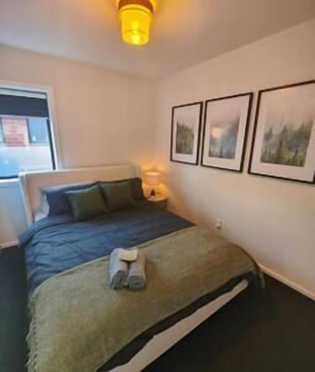 A bedroom with a bed, a bedside table with a lamp, and three framed pictures on the wall.