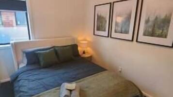 A bedroom with a bed, a bedside table with a lamp, and three framed pictures on the wall.
