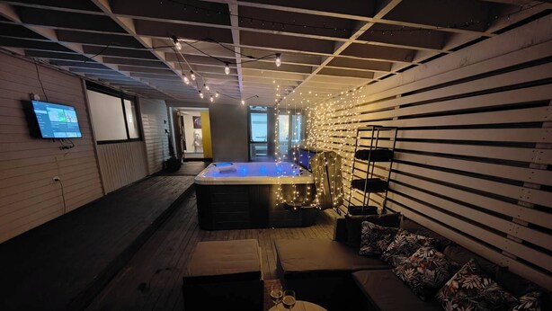 Uma área de estar moderna com hidromassagem, piso de madeira e um espaço de convívio com almofadas.