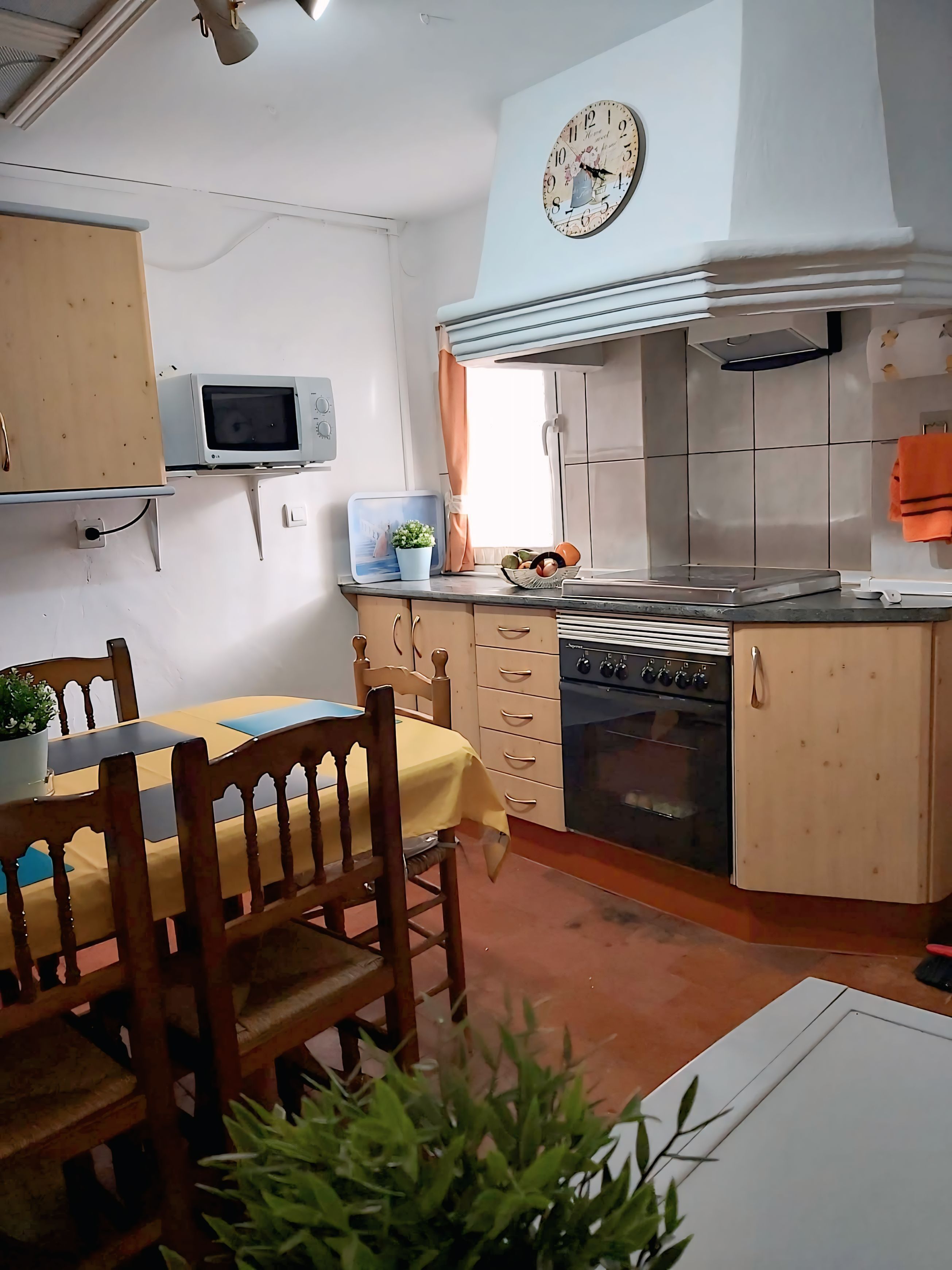 Uma cozinha com uma mesa de jantar, cadeiras, micro-ondas, forno e um relógio na parede.