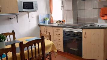 Uma cozinha com uma mesa de jantar, cadeiras, micro-ondas, forno e um relógio na parede.