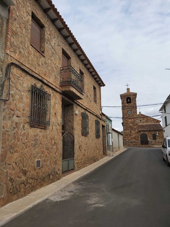 A stone building with a bell tower, a gated entrance, and a paved street.