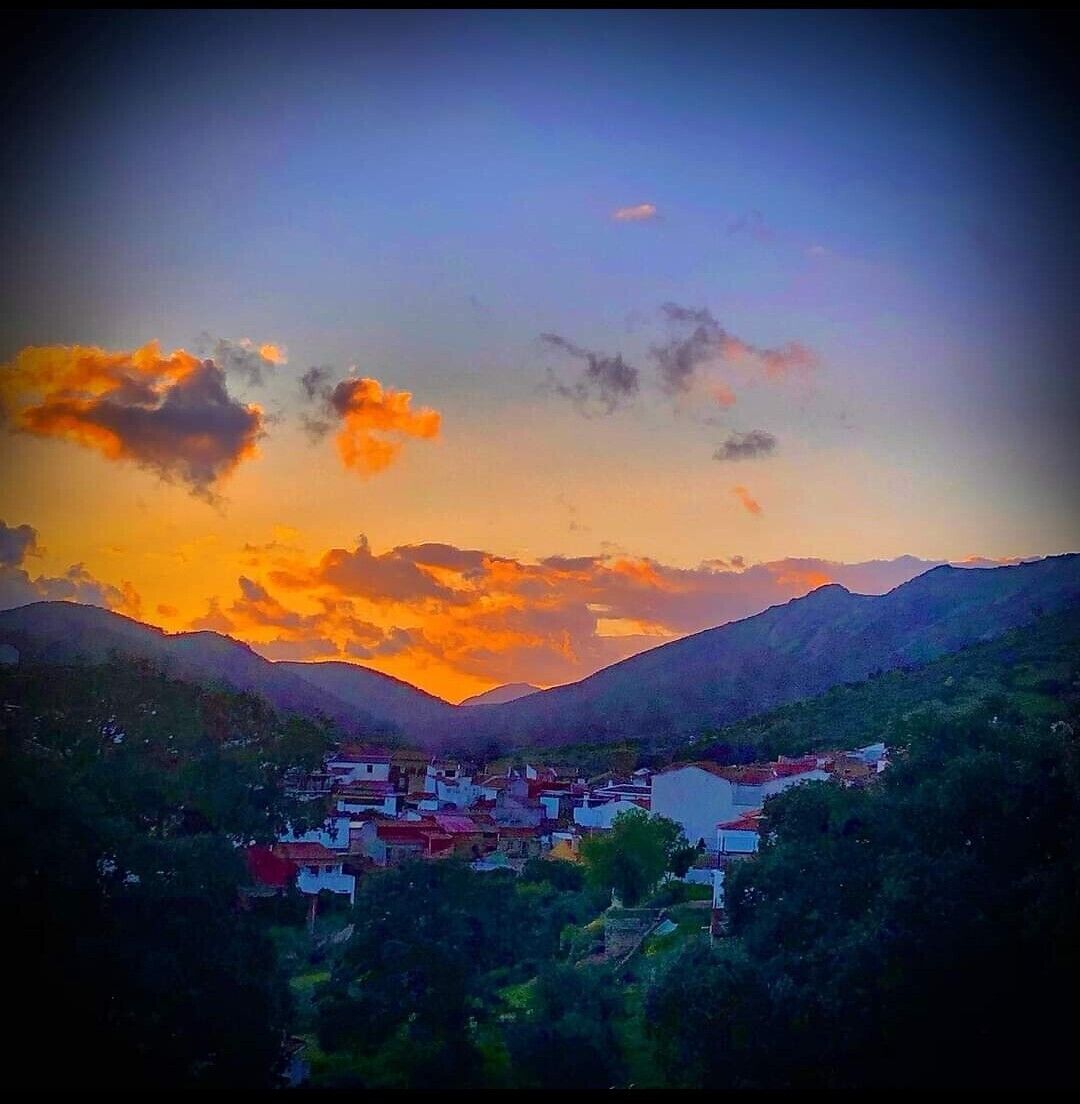 Un pueblo enclavado en un valle, con montañas al fondo, bajo un cielo al atardecer.