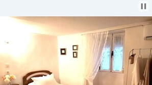 Un dormitorio con una cama individual, una mesita de noche con lámpara, un armario y una ventana con cortinas.