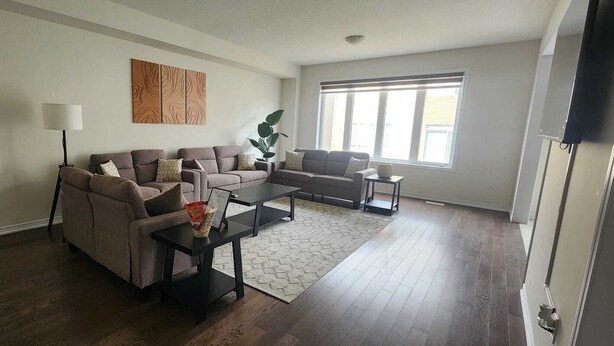 A living room with two sofas, a coffee table, a lamp, and a large window. - Spacious Retreat Near Majestic Niagara Falls! Close to All Major Amenities! (Thorold)
