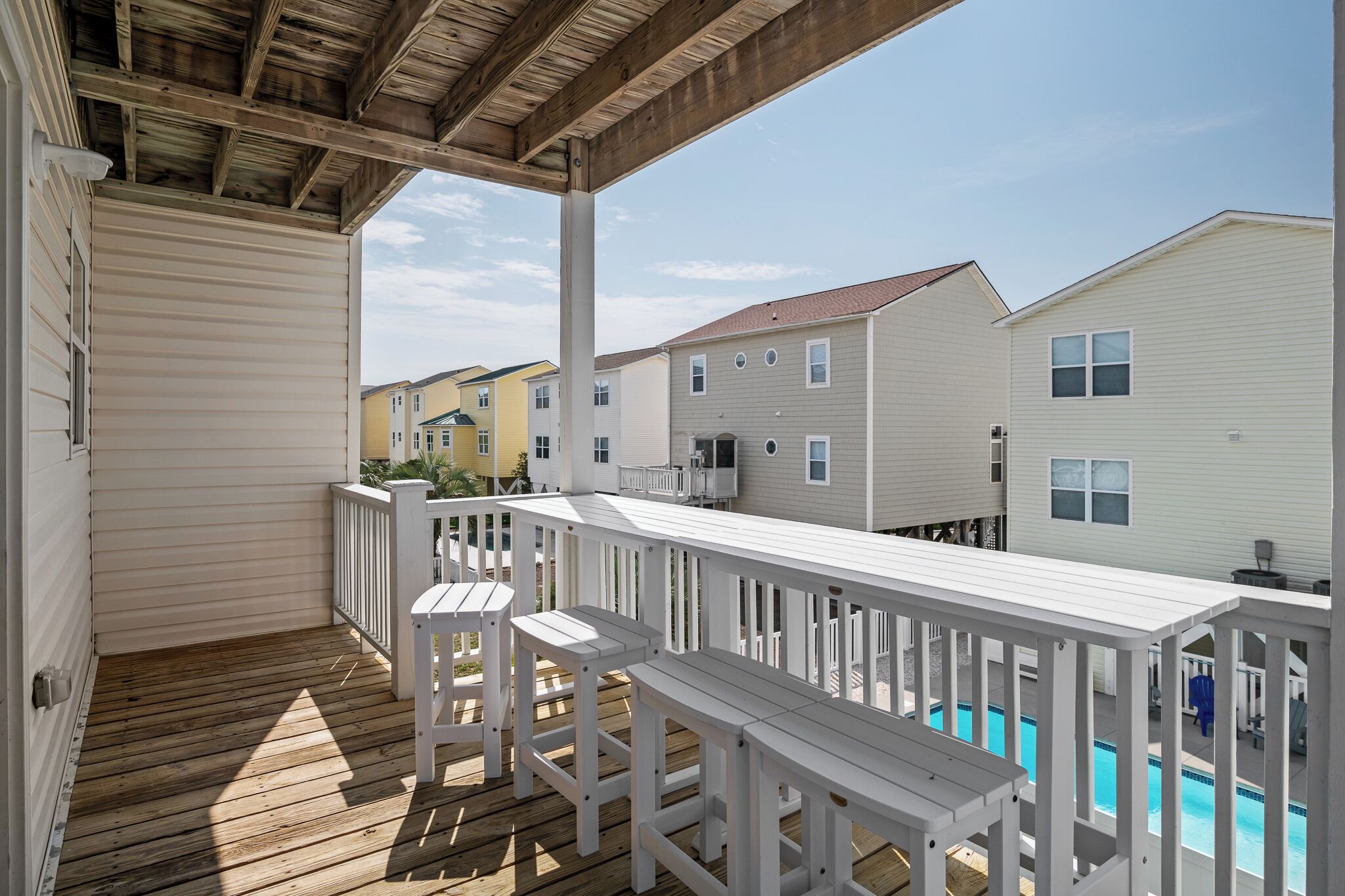 A covered deck with white railings and a pool.
