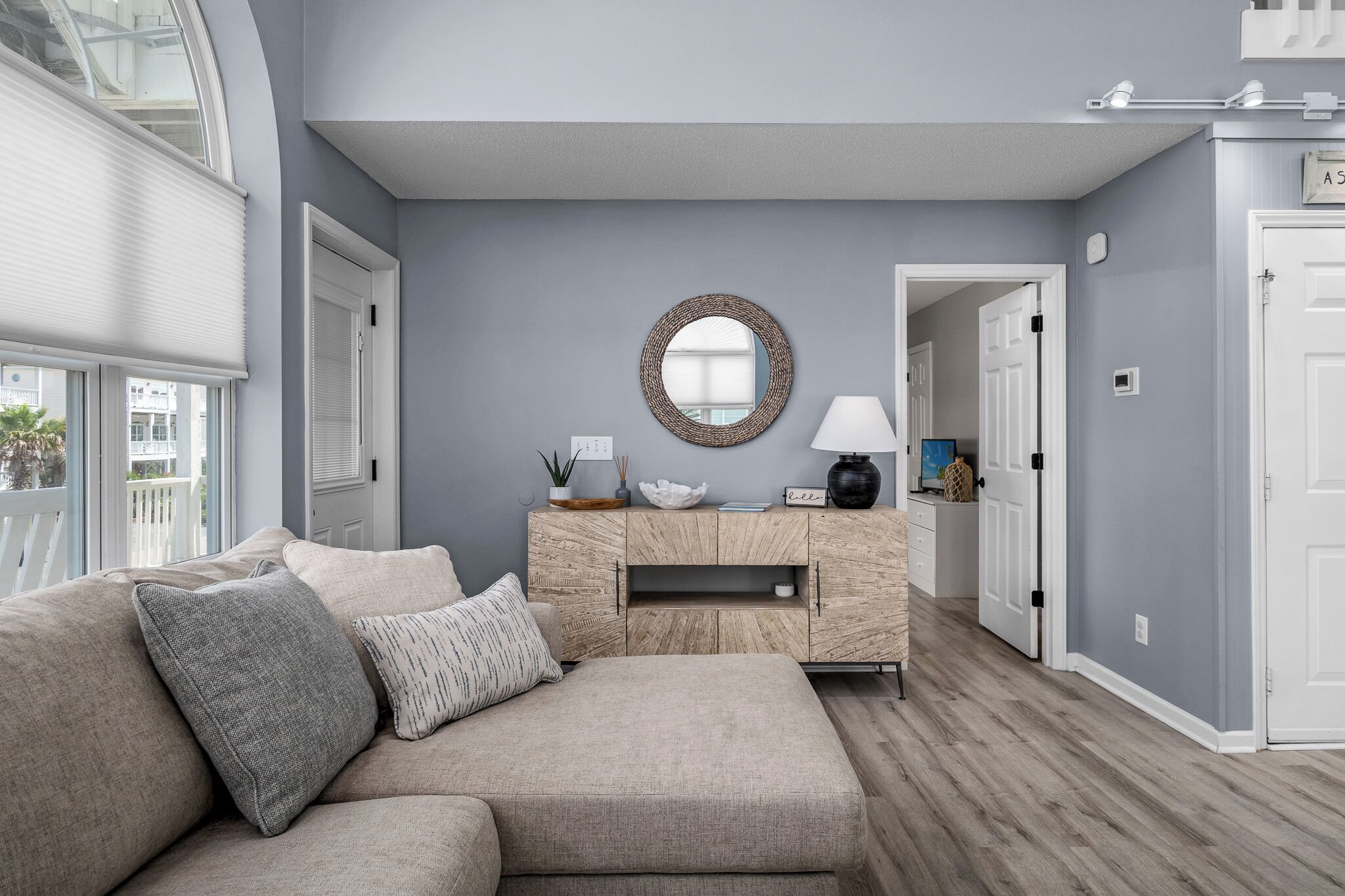 A modern living room with a grey wall, a round mirror, a wooden cabinet, and a beige sofa.