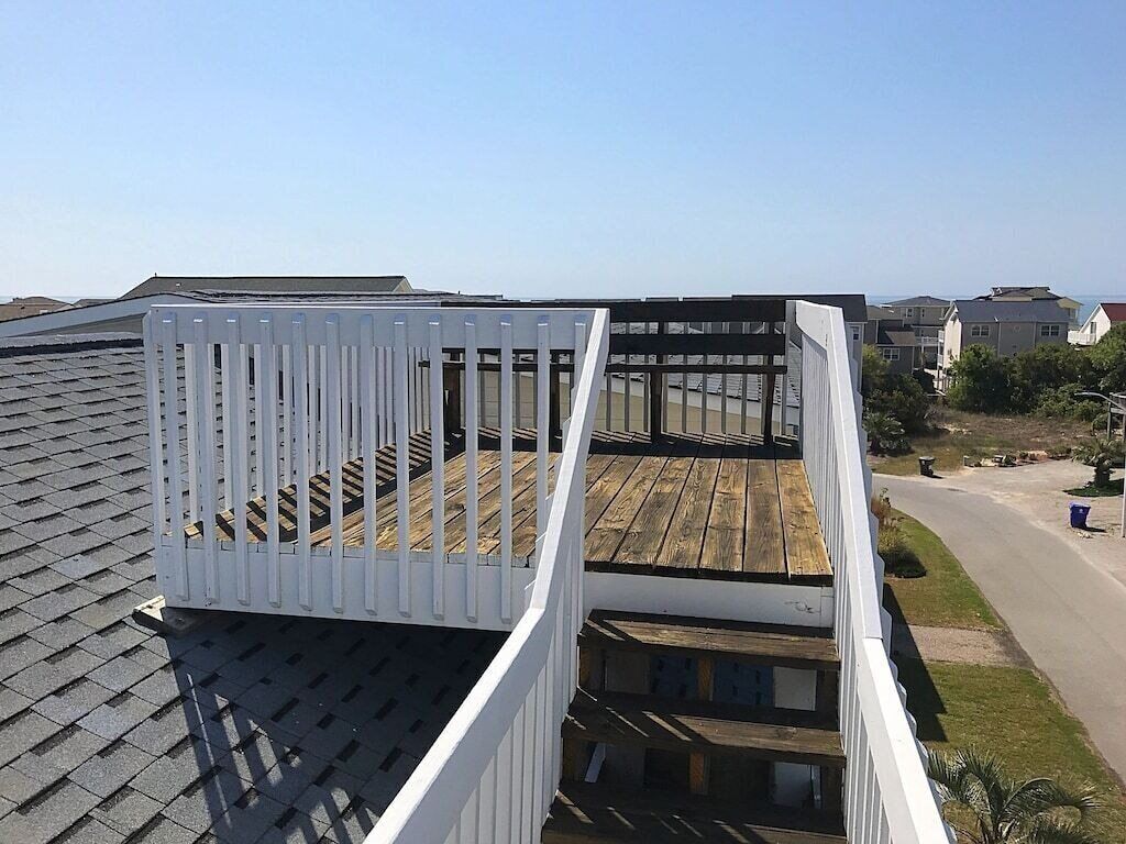 A rooftop with a white railing, a wooden deck, and a view of the surrounding neighborhood.