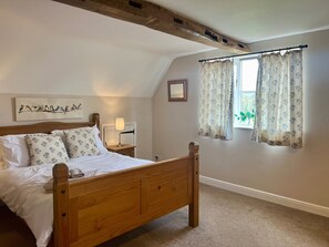 Quarto com cama de madeira, mesa de cabeceira, luminária, quadro emoldurado e janela com cortinas.