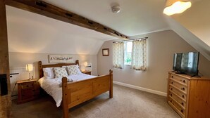 A bedroom with a wooden bed, a nightstand, a dresser, a window with curtains, a ceiling light, and a wall-mounted picture. - Delightful rural country cottage, Great for families and groups, large garden and a big hot tub! (Beccles)