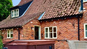 A brick house with a sloped roof, a hot tub, and a deck with outdoor furniture. - Delightful rural country cottage, Great for families and groups, large garden and a big hot tub! (Beccles)
