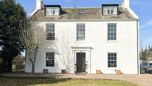 A two-story white building with a central entrance, multiple windows, and a sloped roof. - 9 bedroom accommodation in Kirknewton, near Edinburgh (Kirknewton, near Edinburgh)