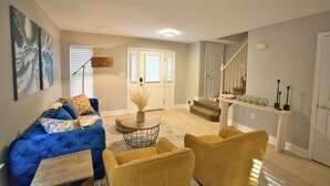A living room with a blue sofa, yellow armchairs, a round coffee table, and a staircase leading to a second floor.