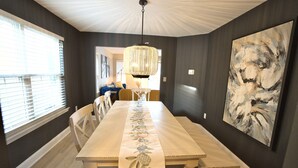 A dining room with a long table, chairs, a chandelier, and a large abstract painting on the wall.