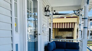 A covered porch with a blue sofa, a welcome mat, and a striped awning.