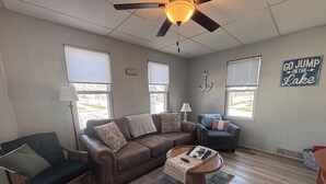 A living room with a brown leather sofa, a wooden coffee table, a dark armchair, and a small side table. - 1 Block to the Beach! Firepit, 2 Bikes, Sleeps 5 (Two Rivers)