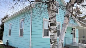 A light blue house with white trim and a front porch. - 1 Block to the Beach! Firepit, 2 Bikes, Sleeps 5 (Two Rivers)