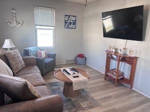 A living room with a brown leather couch, a blue armchair, a coffee table, a TV, and a sign that says 'GO JUMP IN THE LAKE'. - 1 Block to the Beach! Firepit, 2 Bikes, Sleeps 4 (Two Rivers)
