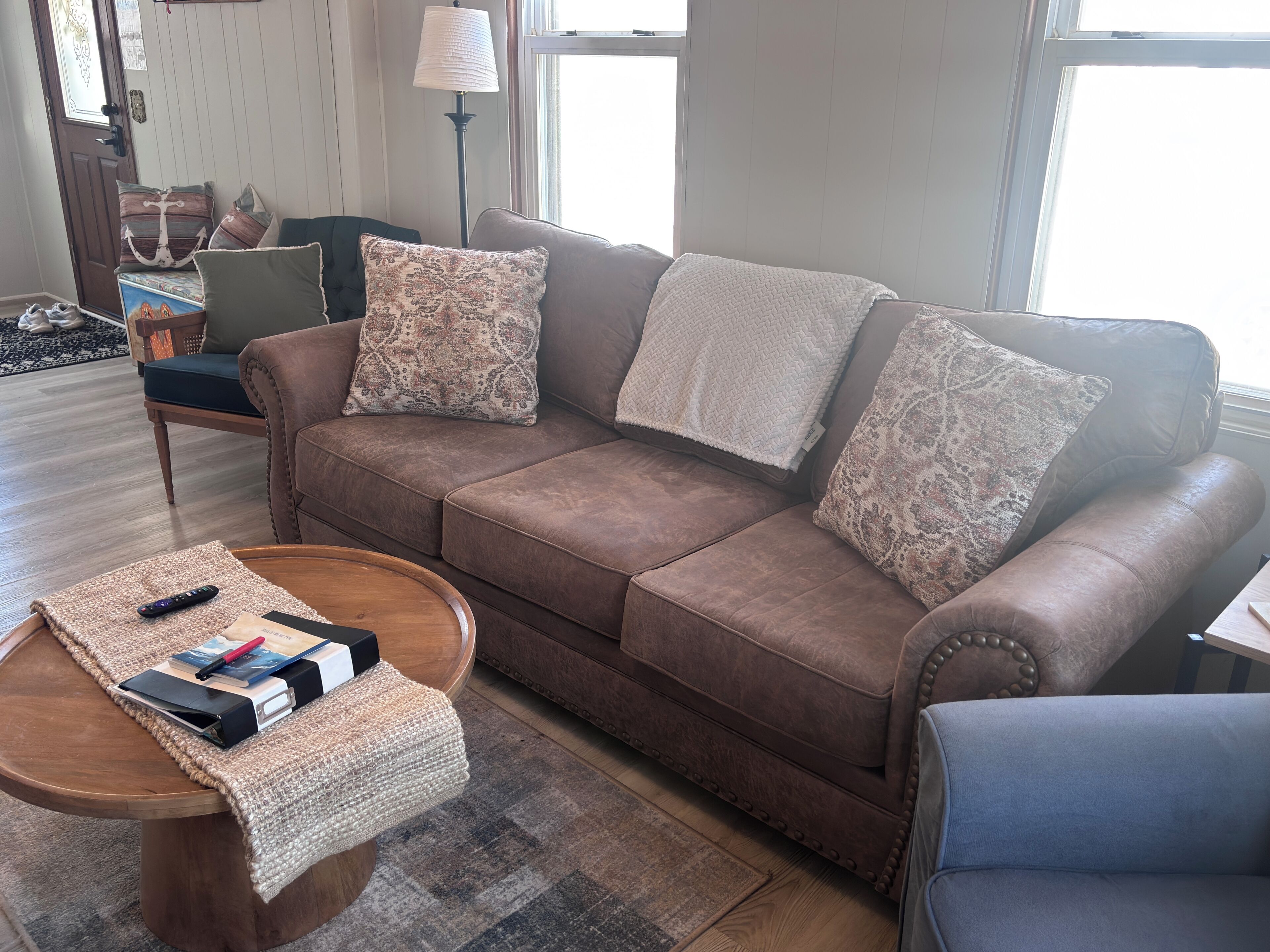 Ein braunes Ledersofa mit gemusterten Kissen, ein Couchtisch aus Holz mit einer gewebten Unterlage und ein blauer Sessel.