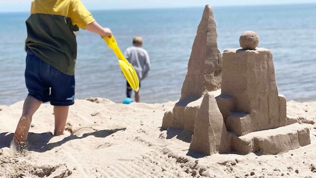 A child playing with sand near a beach with a large sandcastle and a calm sea in the background. - 1 Block to the Beach! Firepit, 2 Bikes, Sleeps 5 (Two Rivers)