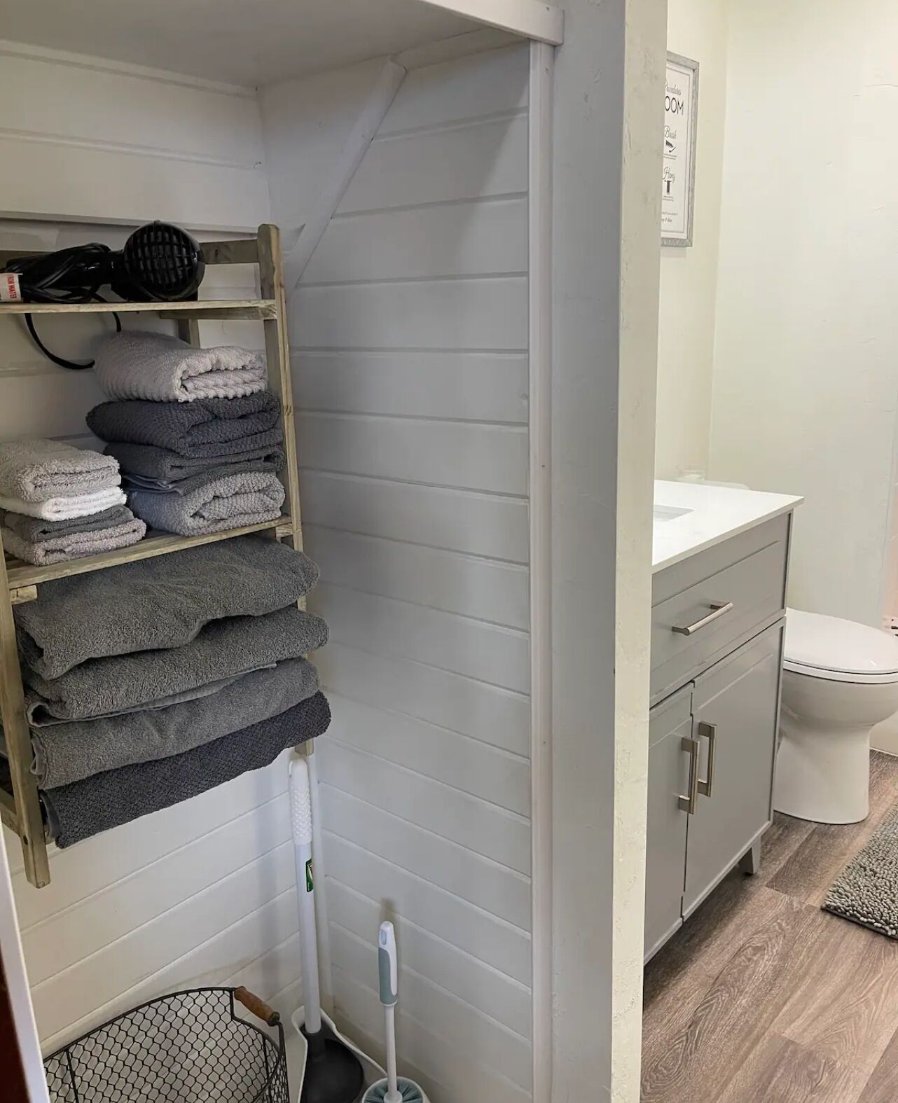 Een badkamer met een wit wastafelmeubel, toilet en een plank met opgevouwen handdoeken.