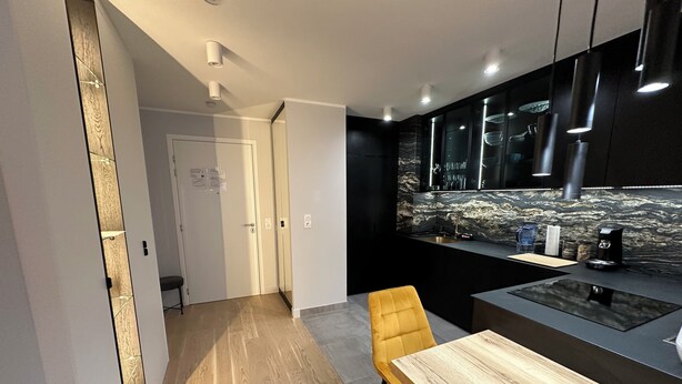 A modern kitchen with a wooden dining table and chairs, a black countertop, and a marble backsplash. - Luxury Apartment Near Paris (Issy-les-Moulineaux)