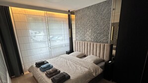 A modern bedroom with a large bed, a headboard, a bedside table, and a wardrobe. - Luxury Apartment Near Paris (Issy-les-Moulineaux)