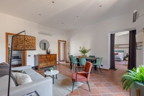Amplia sala de estar con sofá, mesa de comedor, sillas, una mesita de centro, lámpara decorativa y planta en maceta.