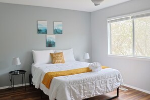 Un dormitorio con una cama, dos mesitas de noche, un ventanal y tres cuadros colgados en la pared.