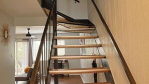 Eine moderne Treppe mit Holzdielen und schwarzen Metallgeländern, die zu einem Bereich im zweiten Stock mit Schreibtisch und Stuhl führt.