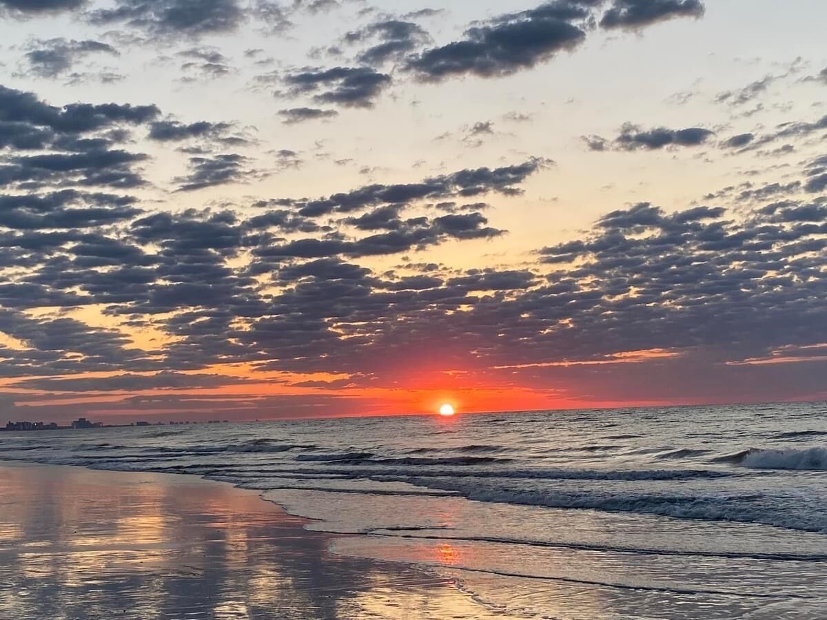 Une plage au coucher du soleil, avec le soleil bas à l’horizon, se reflétant sur l’eau.