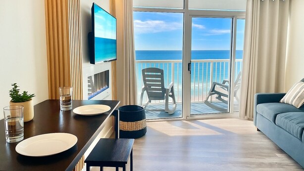 Een moderne hotelkamer met een balkon, een flatscreen televisie, een eettafel met stoelen en een bank.
