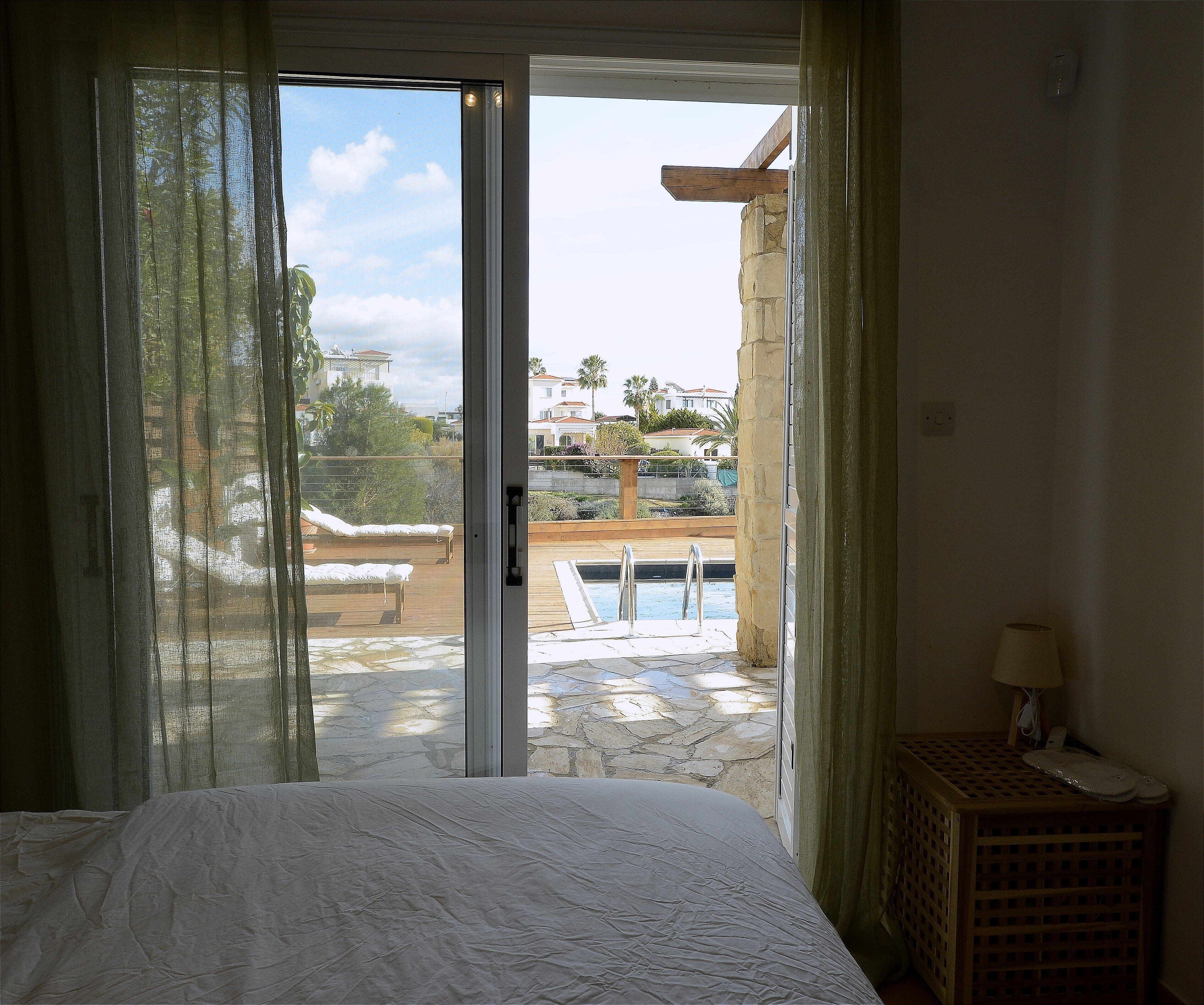 A bedroom with a large bed, a view of a swimming pool, and a balcony with a wooden deck.