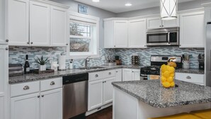 A modern kitchen with white cabinets, a granite countertop, stainless steel appliances, and a window with a view. - The Marina 3BD Townhouse Downtown Beaches Wineries (Traverse City)