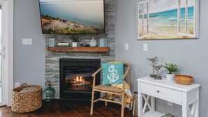 A living room with a fireplace, a television mounted above it, and a beach-themed painting on the wall. - The Marina 3BD Townhouse Downtown Beaches Wineries (Traverse City)