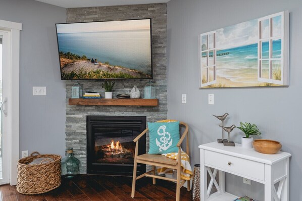 A living room with a fireplace, a television mounted above it, and a beach-themed painting on the wall.