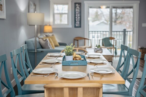 Een eetruimte met een houten tafel gedekt voor zes personen, blauwe stoelen, een kleine potplant en een blauwe dienblad met eten.