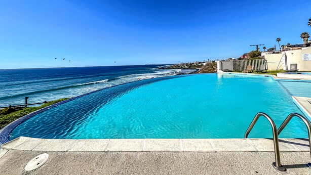 A clear blue pool with a view of the ocean and a distant shoreline.