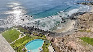 A coastal view with a swimming pool, beach, and rocky shoreline.