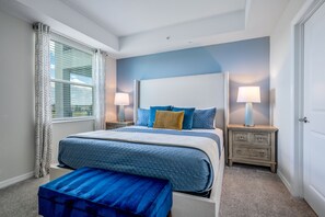 Ein Schlafzimmer mit einem Bett, zwei Nachttischen, einer Bank und einem Fenster mit Vorhängen.
