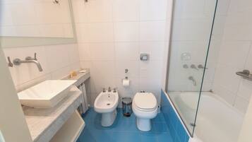 Une salle de bain équipée d’un bidet, de toilettes, d’un lavabo et d’une douche à parois en verre.