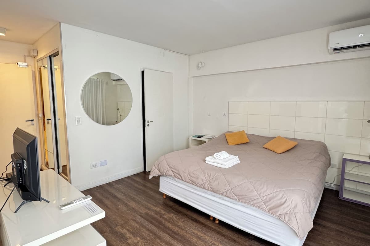 A modern bedroom with a large bed, a bedside table, a TV, and a mirror.