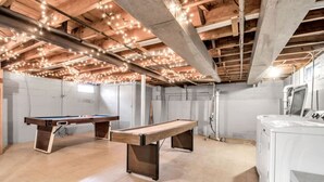 Una habitación amplia con una mesa de billar, otra mesa y una lavadora.