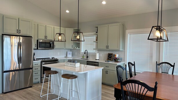 A modern kitchen with stainless steel appliances, white cabinetry, and a central island with stools. - Beautiful home on the river, mins to the Gulf; fire-pit, bar, view  (Steinhatchee)