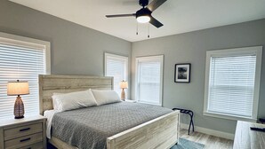 A bedroom with a wooden bed, two bedside tables with lamps, a ceiling fan, and large windows with blinds. - Beautiful home on the river, mins to the Gulf; fire-pit, bar, view  (Steinhatchee)