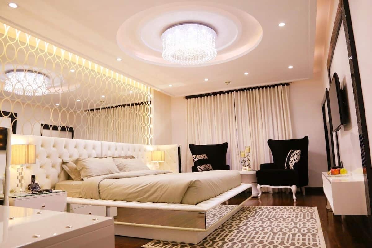 A modern bedroom with a large bed, bedside tables, a chandelier, and a patterned rug.