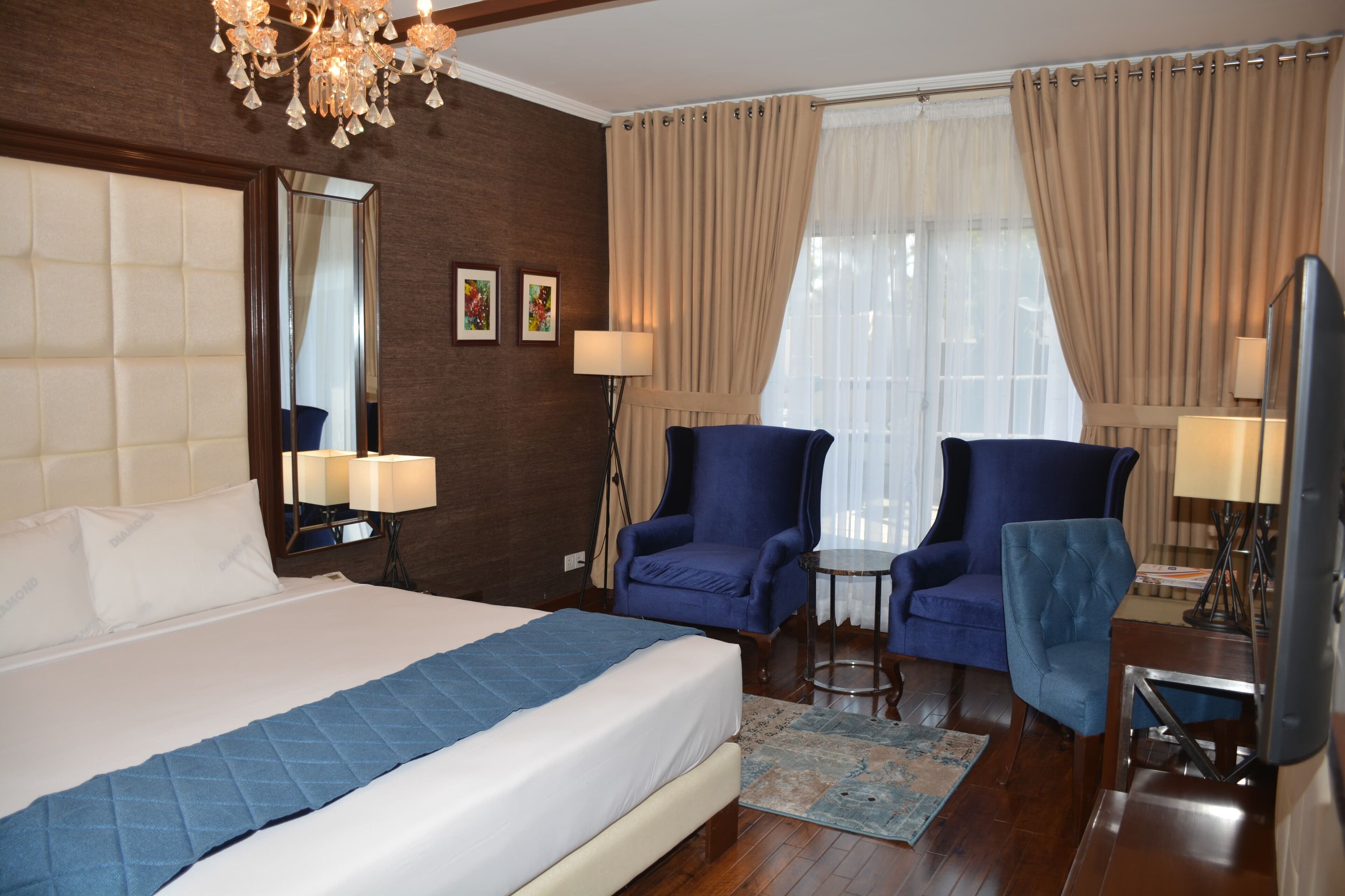 Camera d'albergo con un letto grande, due poltrone, un tavolino, una TV e un lampadario.