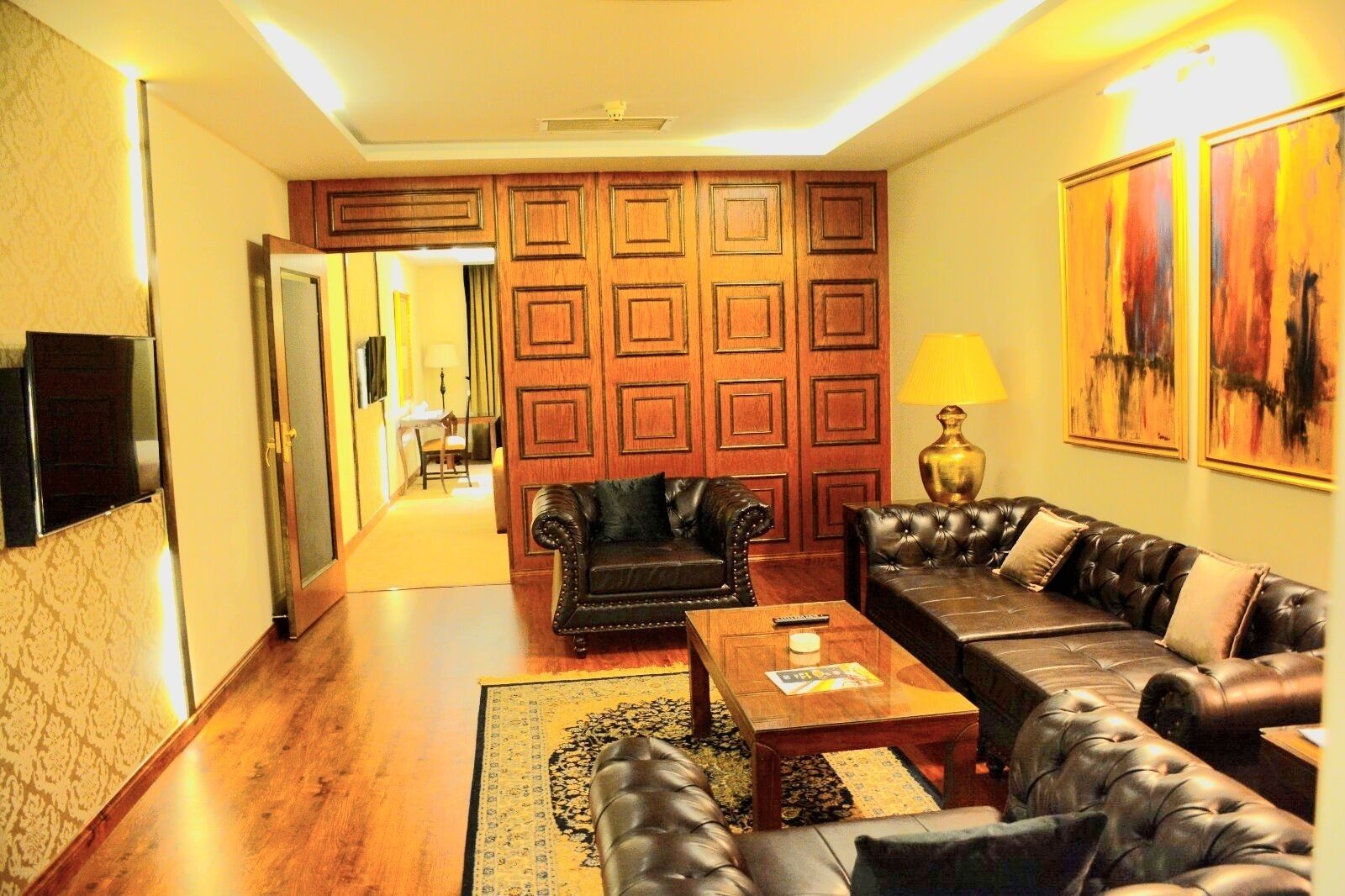 Una sala de estar con un panel de pared de madera, sofás de cuero, una mesa de centro y un televisor a la izquierda.